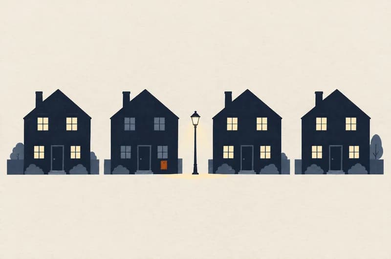Fire huse langs en vej om aftenen, hvor tre har lys i vinduerne og det andet fra venstre står helt mørkt med en orange eltavle på facaden, mens gadelampen imellem dem lyser